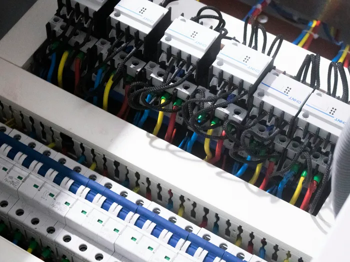 Close-up inside a distribution board, rows of circuit breakers and contactors wired in red, yellow, blue and black